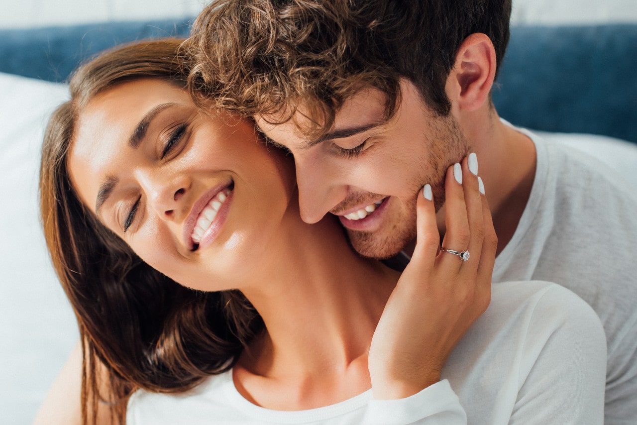 a smiling couple with the woman wearing an engagement ring