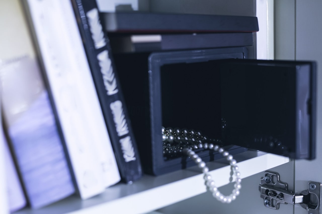 Beautiful pearl necklaces inside a small jewelry safe, nestled between books on a shelf.