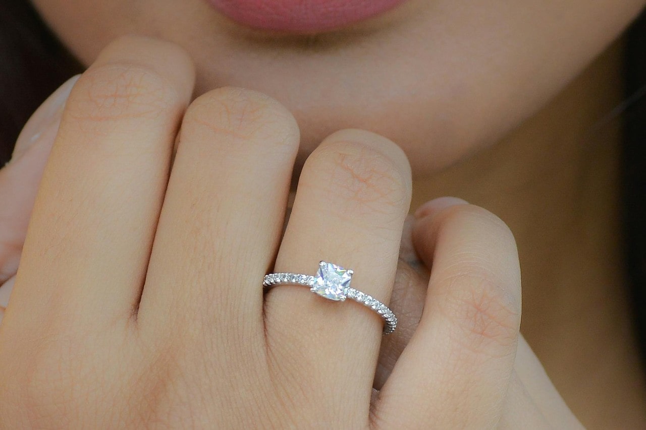 A close-up of a woman’s hand wearing an elegant engagement ring.