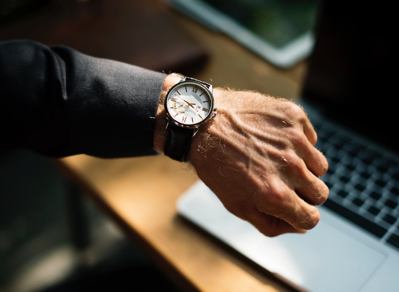 A well-dressed man checking his watch as he works at a desk.