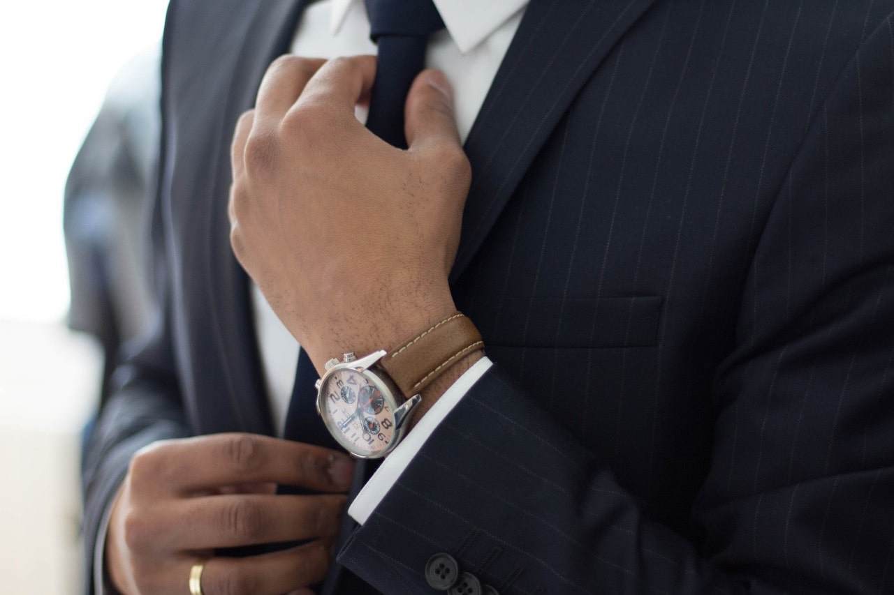 A well-dressed man in a suit straightening his tie, an authentic watch on his wrist.