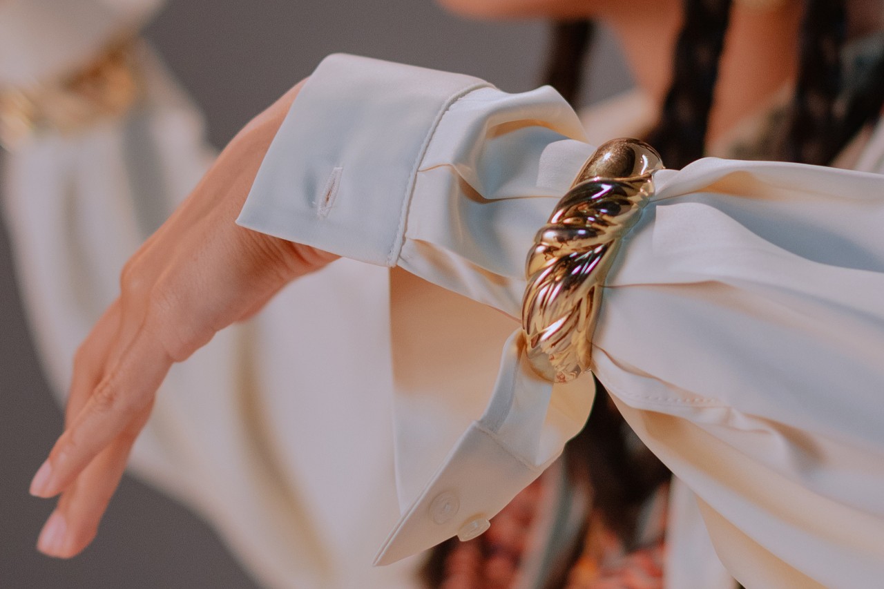 a woman’s arm wearing a white sleeve and a bold gold cuff bracelet