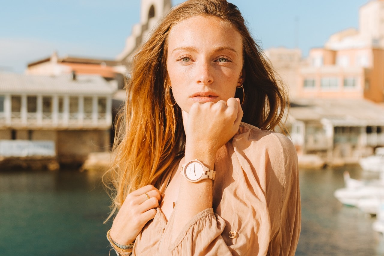 A woman wearing a watch as the wind blows off a river on vacation.