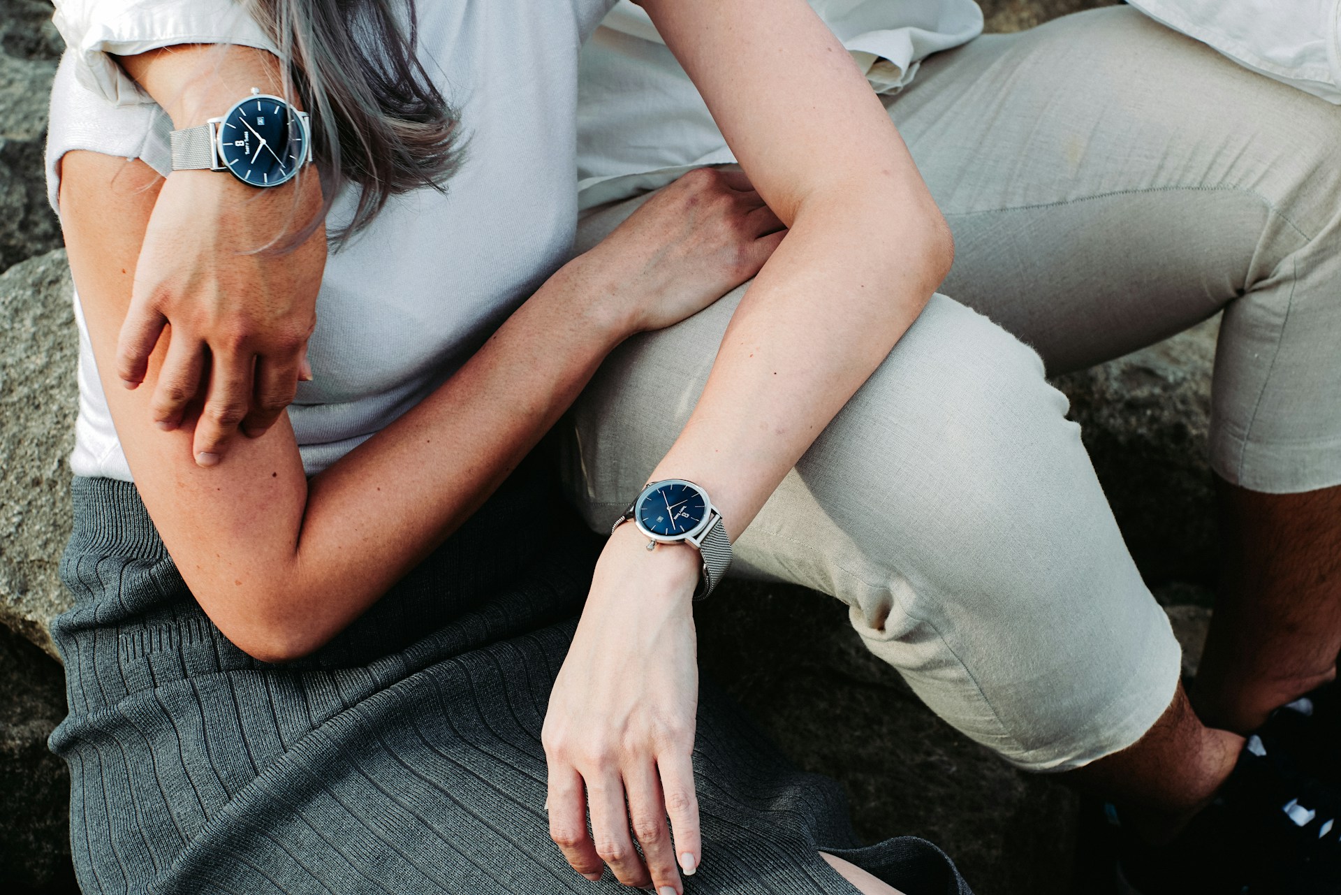 a couple sitting together outdoors wearing matching silver and blue watches