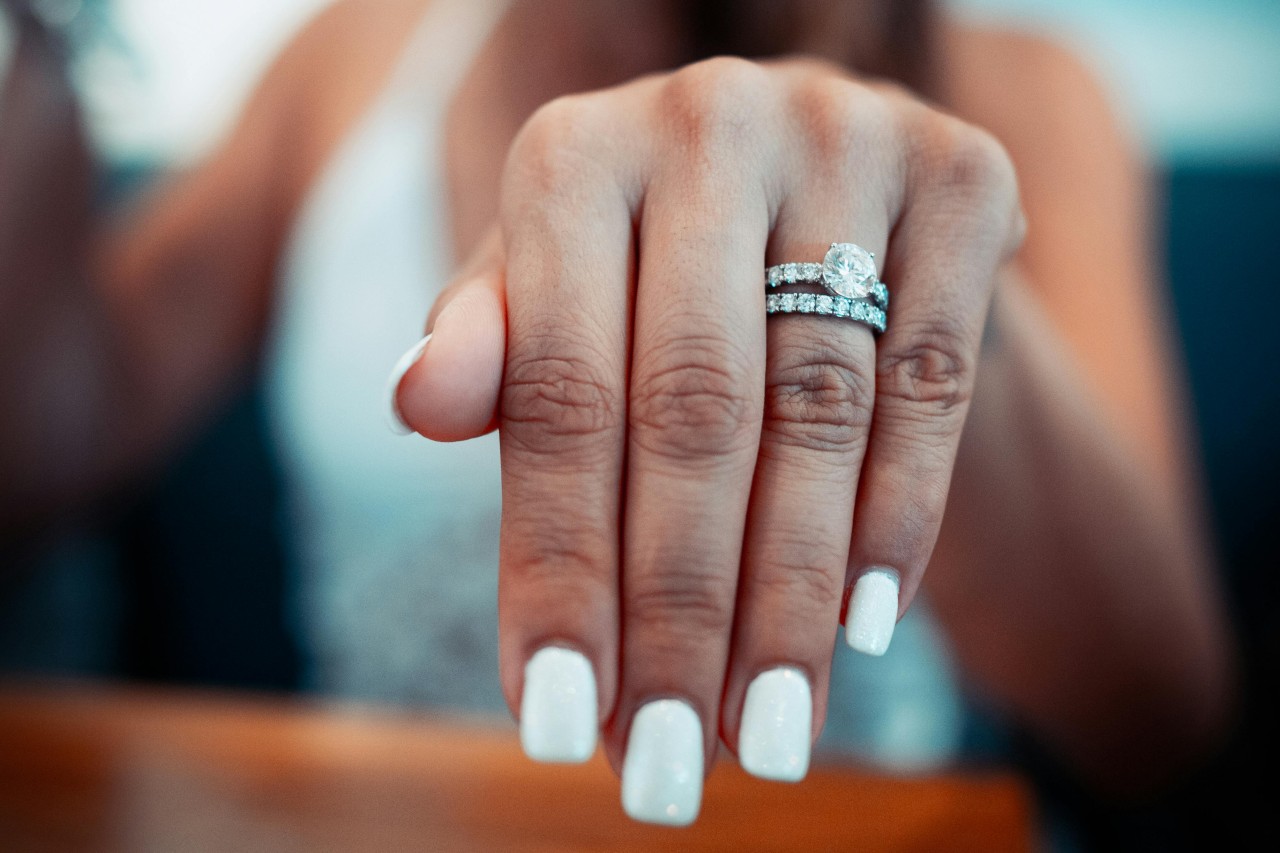 A close-up of a woman’s extended hand adorned with a round cut engagement ring and diamond wedding band.