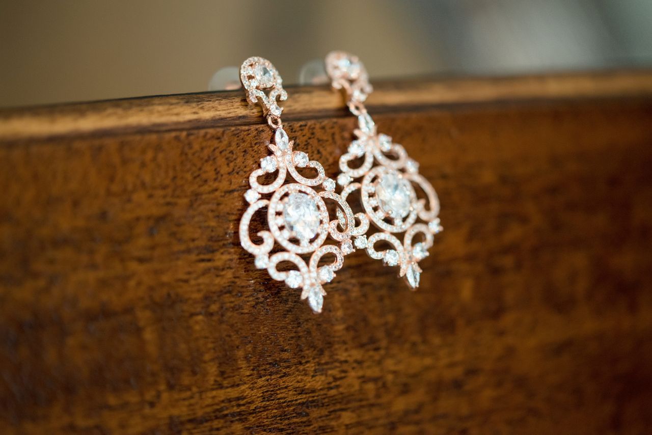 An ornate pair of diamond earrings displayed on a wooden vanity front.