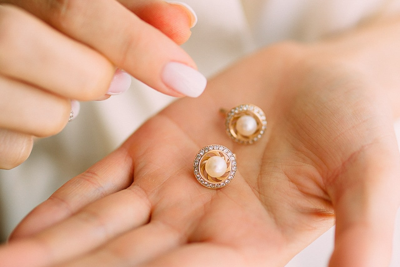 A woman holding a pair of diamond and pearl stud earrings in the palm of her hand.